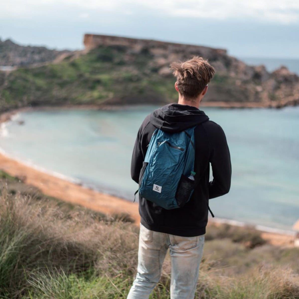 Packable Daypack 20 L in solid blue, worn by the sea